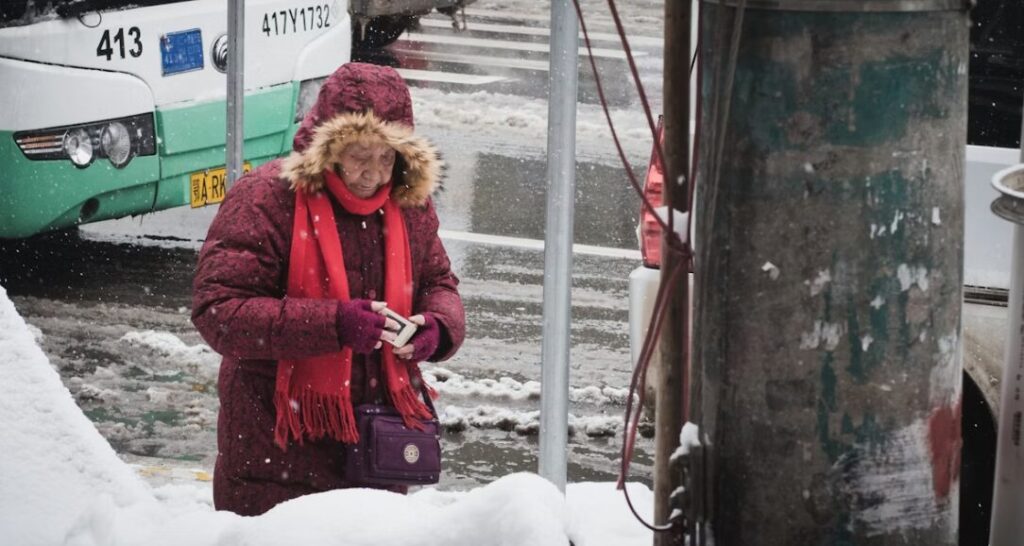 노인분이 추운 한파에 목도리를 두르시고 길가에서 핸드폰을 만지고 있으시는 이미지